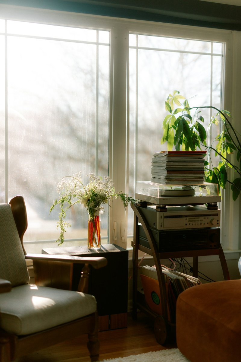 Fauteuil, plantes et pile de livres devant une grande fenêtre lumineuse