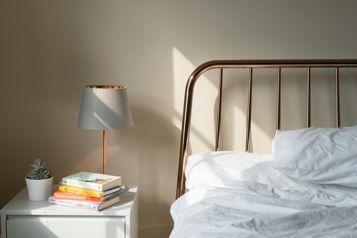 Lit à tête de lit métallique, lampe de chevet et livres sur la table de nuit