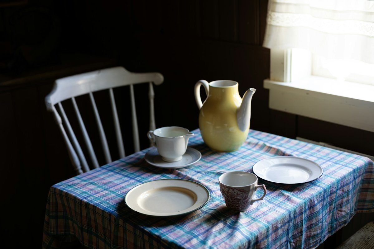Table de cuisine à nappe à carreaux, pichet jaune et tasses près d'une fenêtre
